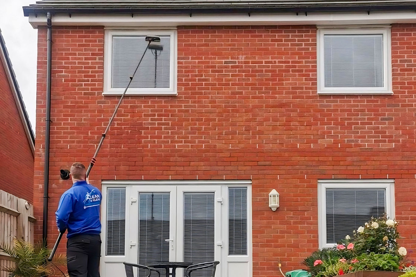 Man cleaning top floor windows with large pole on a residential house.