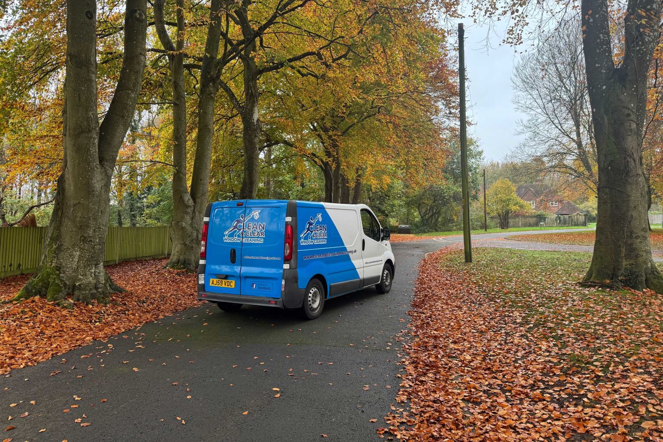 Clean and clear window cleaning van on a path with autumn leaves either side.